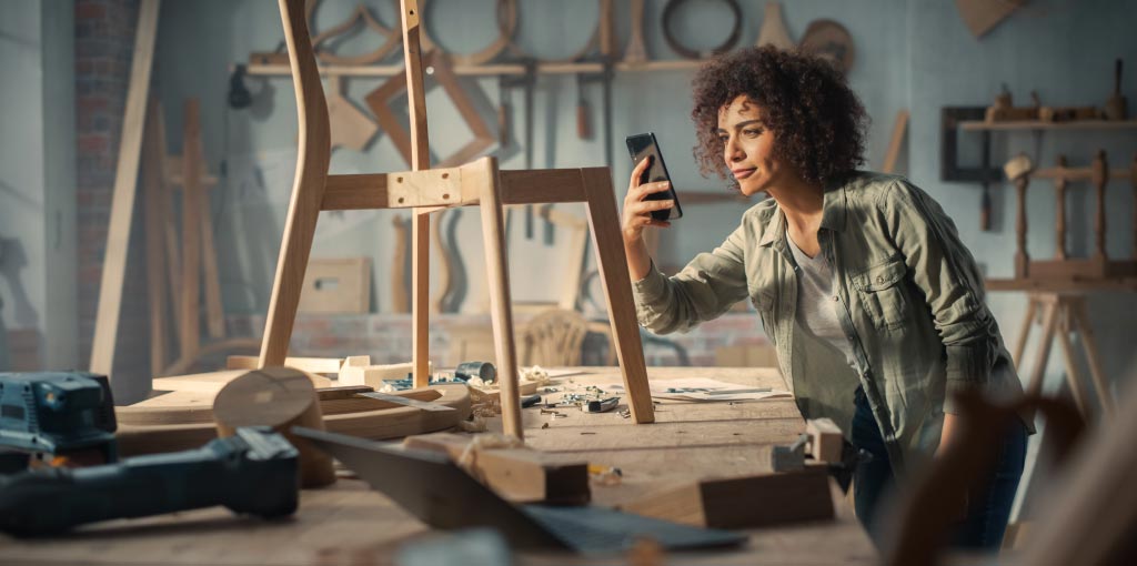 Ragazza che fotografa una sedia in legno in lavorazione in una falegnameria