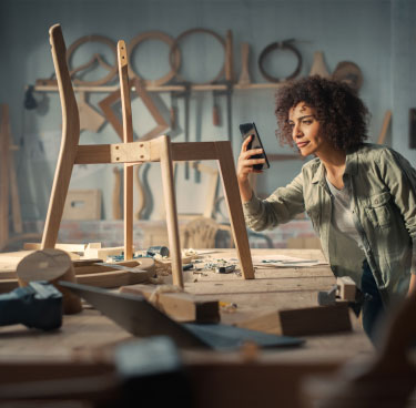 Ragazza che fotografa una sedia in legno in lavorazione in una falegnameria